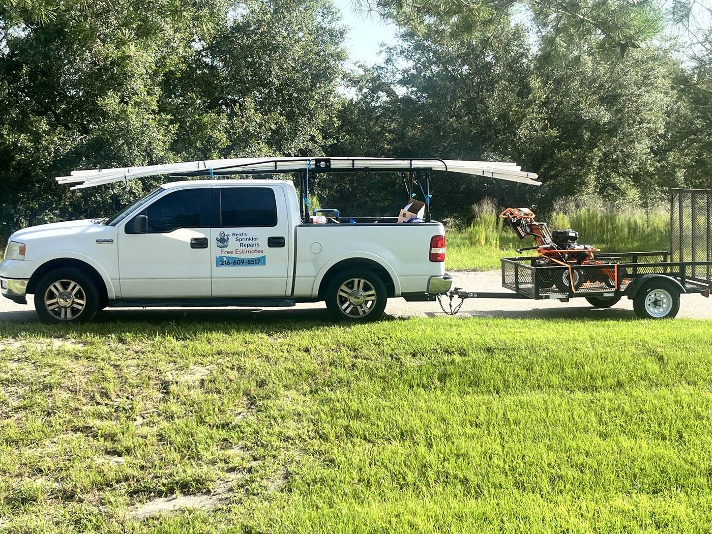 Reid's Sprinkler Repairs truck and equipment trailer parked on a grass shoulder
