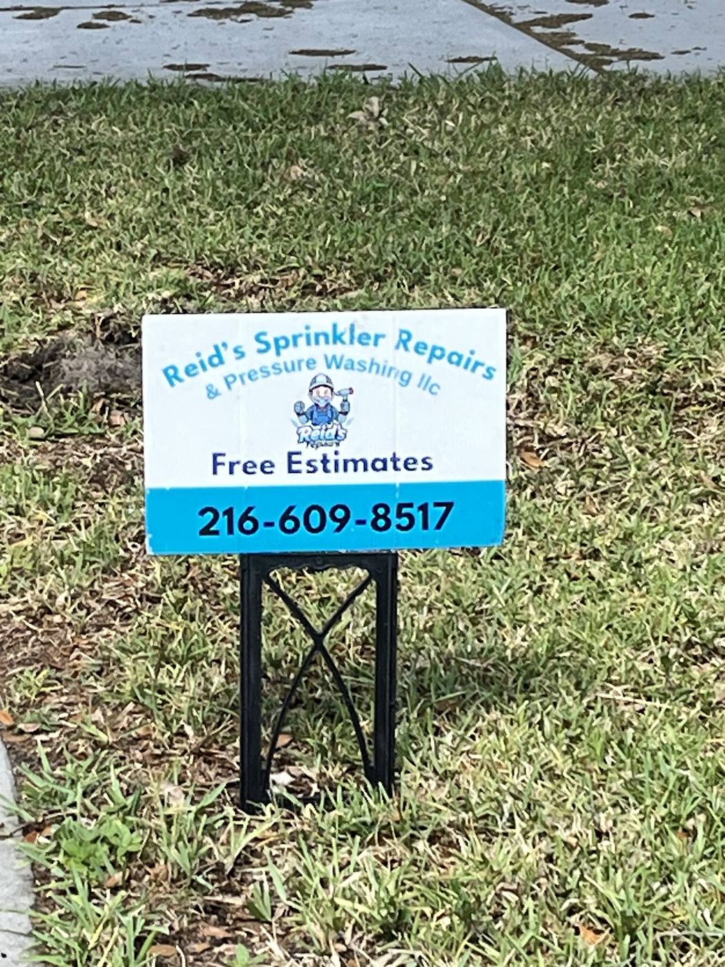 Reid's Sprinkler Repairs yard sign with phone number, placed in a client's lawn